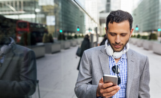 Geschäftsmann mit Kopfhörer und Mobiltelefon in der Stadt - MGOF03514