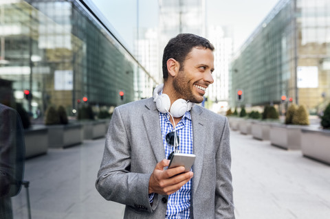 Smiling businessman with headphones and cell phone in the city stock photo