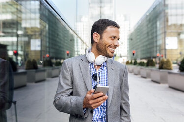 Smiling businessman with headphones and cell phone in the city - MGOF03515