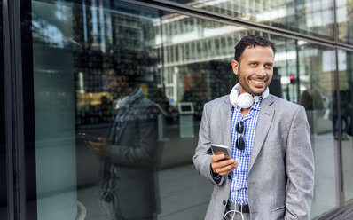 Smiling businessman with headphones and cell phone in the city - MGOF03516