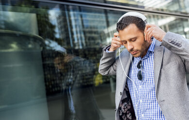 Businessman putting on headphones in the city - MGOF03517