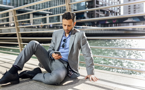 Geschäftsmann sitzt auf einer Brücke mit Handy in der Stadt, lizenzfreies Stockfoto