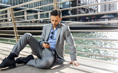 Businessman sitting on a bridge with cell phone in the city - MGOF03526