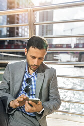 Businessman sending messages with his smartphone in the city - MGOF03527