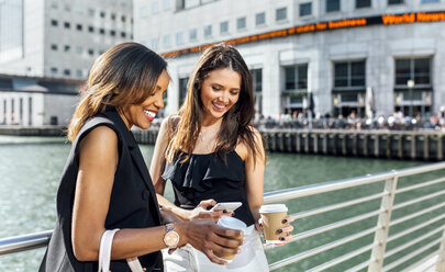 Zwei Frauen auf einer Brücke mit Kaffee zum Mitnehmen und Mobiltelefon - MGOF03530