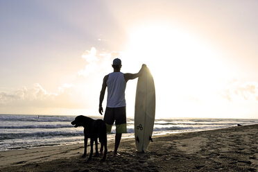 Rückenansicht eines Mannes mit Surfbrett und Hund bei Sonnenuntergang am Strand - ECPF00007
