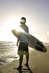 Mann mit Surfbrett steht am Strand und beobachtet den Sonnenuntergang - ECPF00009