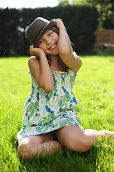Glückliches verspieltes Mädchen mit Hut im Garten sitzend - ECPF00037