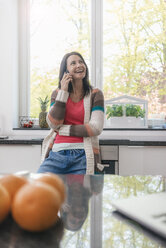 Lächelnde Frau in der Küche beim Telefonieren - JOSF01249