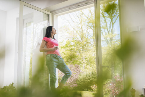 Frau steht in der Küche auf der Fensterbank - JOSF01250