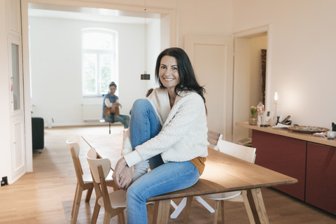 Porträt einer lächelnden Frau, die zu Hause auf einem Tisch sitzt, lizenzfreies Stockfoto