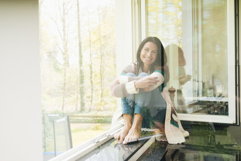 Porträt einer lächelnden Frau zu Hause auf der Fensterbank, lizenzfreies Stockfoto
