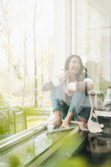Lachende Frau zu Hause auf der Fensterbank sitzend - JOSF01256