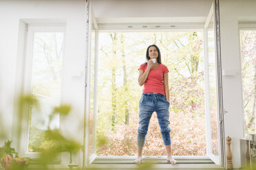 Lächelnde Frau in der Küche auf der Fensterbank stehend - JOSF01259