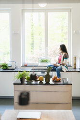 Frau in der Küche schaut aus dem Fenster - JOSF01263
