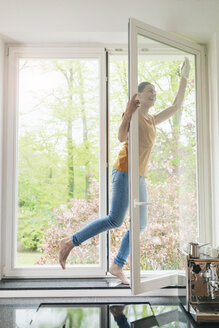 Glückliche Frau steht auf der Fensterbank und putzt das Fenster - JOSF01266