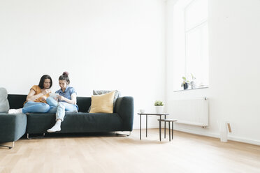 Two women at home sitting on couch looking at photos - JOSF01273