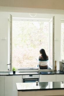 Woman in kitchen sitting on windowsill - JOSF01292
