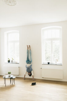 Frau zu Hause macht einen Handstand an der Wand - JOSF01298