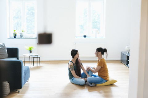 Zwei Frauen, die zu Hause auf dem Holzboden sitzen und sich unterhalten, lizenzfreies Stockfoto