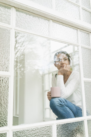 Nachdenkliche Frau mit einer Tasse Kaffee und Blick aus dem Fenster, lizenzfreies Stockfoto