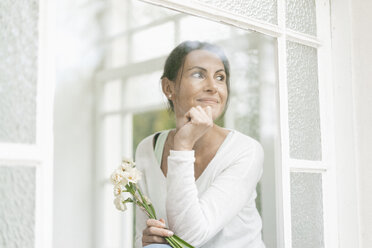 Lächelnde Frau mit Blumen aus dem Fenster - JOSF01311