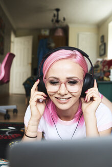 Young woman with pink hair listening to music via laptop at home - IGGF00059