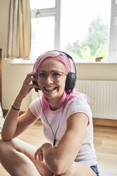 Happy young woman with pink hair listening to music - IGGF00065