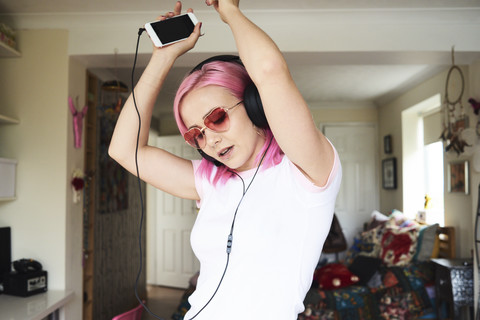 Enthusiastic young woman with pink hair listening to music at home stock photo