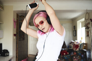 Enthusiastic young woman with pink hair listening to music at home - IGGF00069