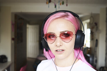 Portrait of young woman with pink hair and heart-shaped sunglasses listening to music - IGGF00070