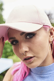 Portrait of young woman with pink hair and piercings wearing cap - IGGF00071