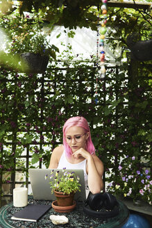 Young woman with pink hair using laptop in cozy garden - IGGF00072