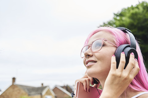 Junge Frau mit rosa Haaren hört im Freien Musik, lizenzfreies Stockfoto