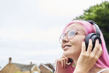 Junge Frau mit rosa Haaren hört im Freien Musik - IGGF00076