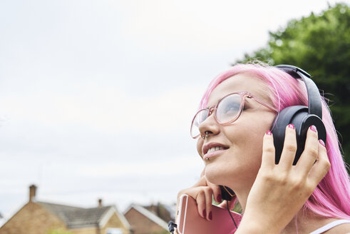 Young woman with pink hair listening to music outdoors - IGGF00076