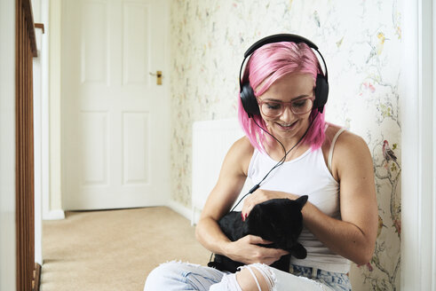Glückliche junge Frau mit schwarzer Katze, die zu Hause Musik hört - IGGF00077