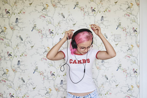 Begeisterte junge Frau mit rosa Haaren hört zu Hause Musik, lizenzfreies Stockfoto