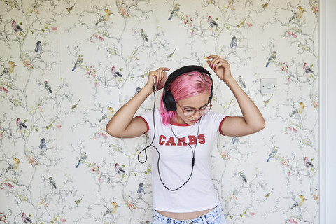 Enthusiastic young woman with pink hair listening to music at home stock photo