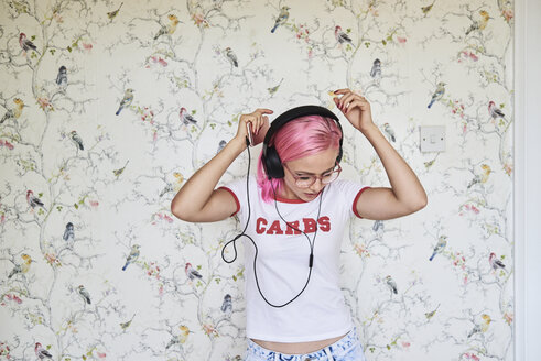 Enthusiastic young woman with pink hair listening to music at home - IGGF00078