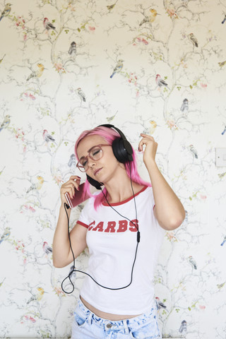 Begeisterte junge Frau mit rosa Haaren hört zu Hause Musik, lizenzfreies Stockfoto