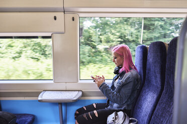 Junge Frau mit rosa Haaren, die während einer Zugfahrt ein Mobiltelefon benutzt - IGGF00080
