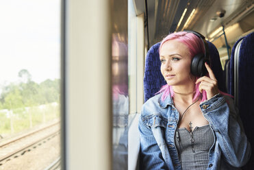 Junge Frau mit rosa Haaren hört Musik während einer Zugfahrt - IGGF00082