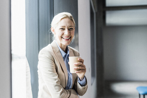 Portrait of happy businesswoman with coffee at the window - UUF11392