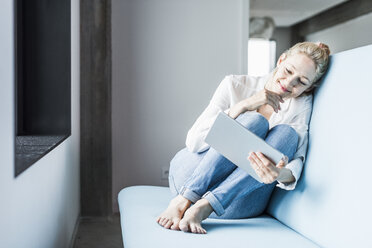 Smiling woman sitting on couch using tablet - UUF11431