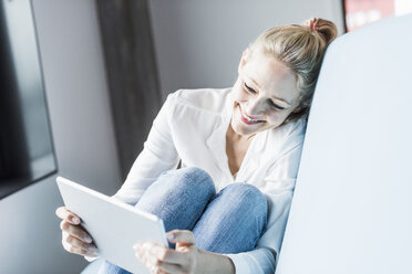 Smiling woman sitting on couch using tablet - UUF11432