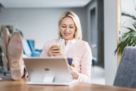 Geschäftsfrau hält Smoothie und benutzt Handy im Büro, lizenzfreies Stockfoto