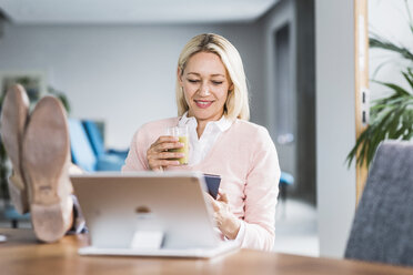 Geschäftsfrau hält Smoothie und benutzt Handy im Büro - UUF11449