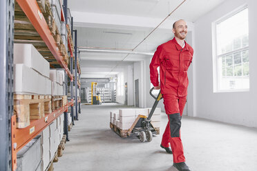 Smiling man in warehouse pulling pallet jack - RHF02024