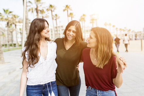 Drei glückliche Freundinnen schlendern über die Strandpromenade - GIOF03001